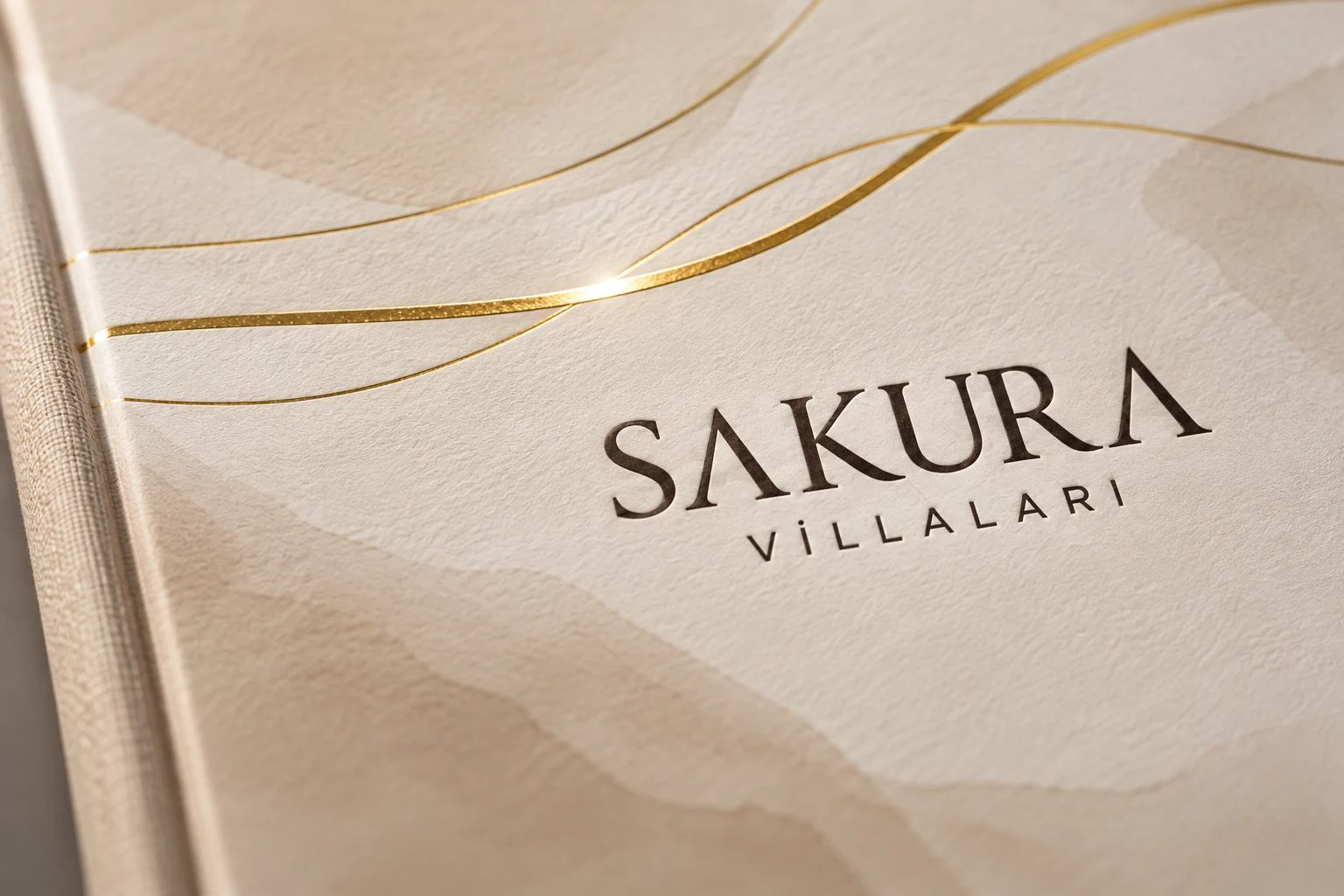 Katalog kapağına yakın bakış: krem suluboya zeminde koyu kahve Sakura Villaları logosu ve üstünden geçen altın yaldız çizgiler