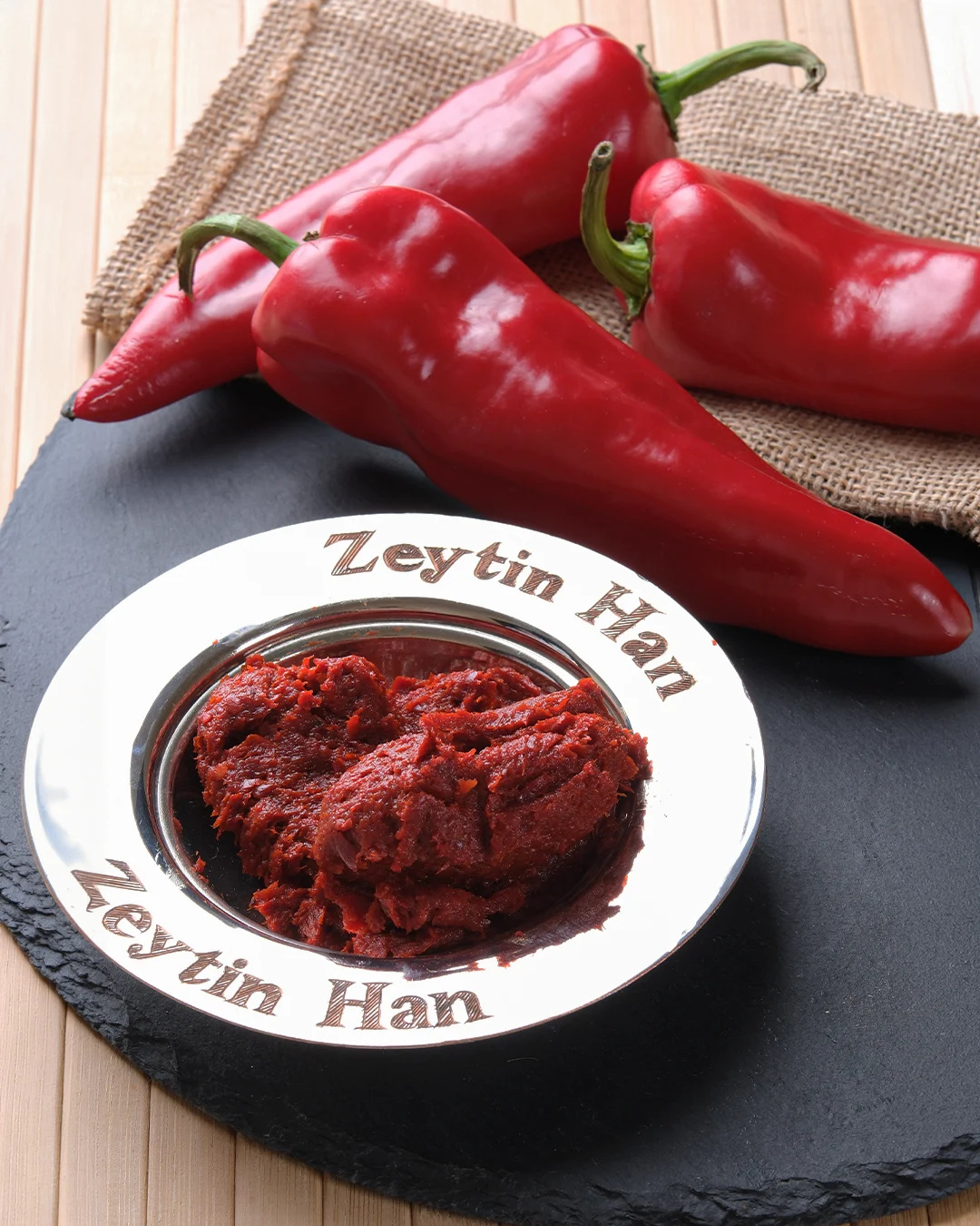 Kırmızı biberlerin önünde “Zeytin Han” tabağında biber salçası