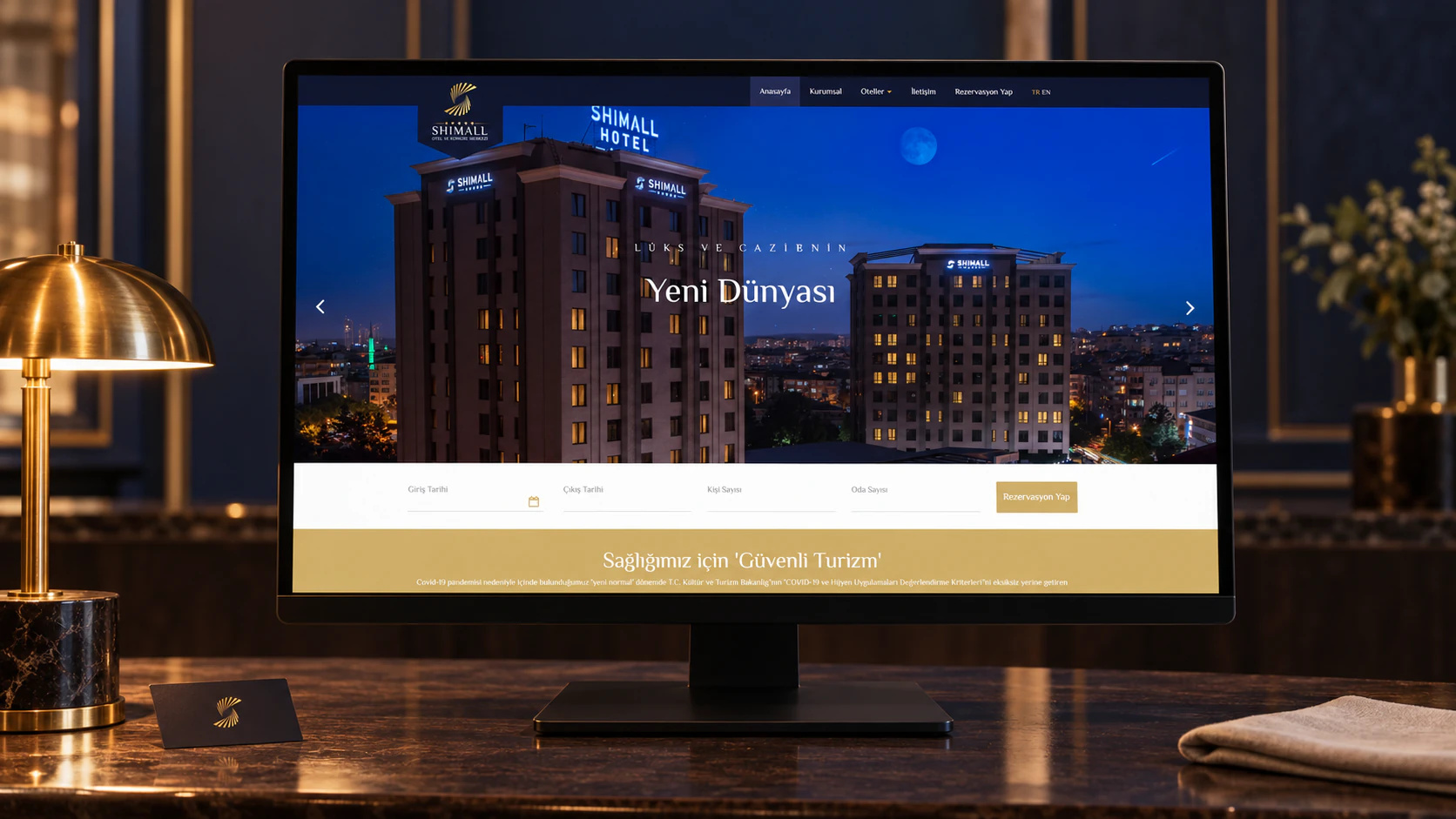 Ahşap resepsiyon masasında Shimall Hotel ana sayfasını gösteren ekran, yanında pirinç masa lambası ve oda kartı