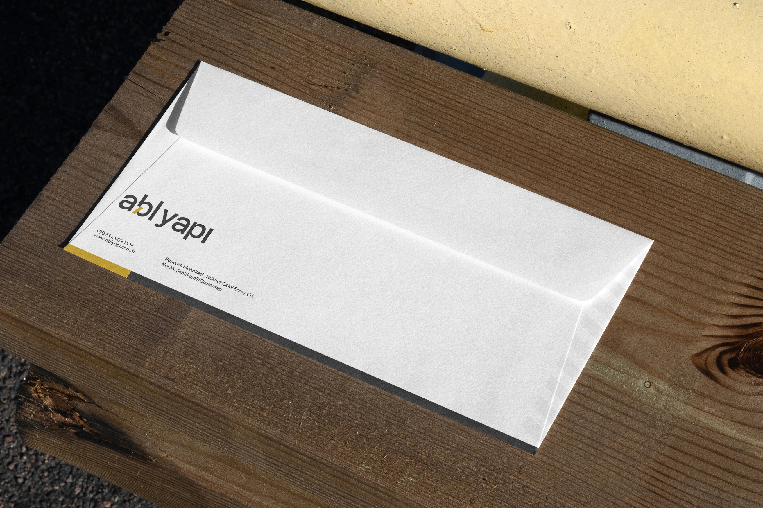 A white ABL Yapı envelope with a yellow band at its corner, on a wooden plank