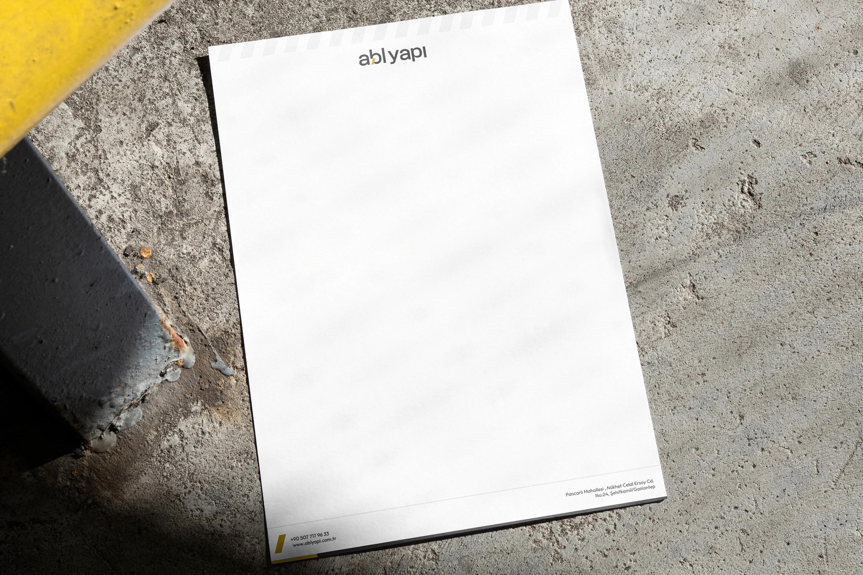 An ABL Yapı letterhead with diagonal stripes along its top edge, on a concrete floor