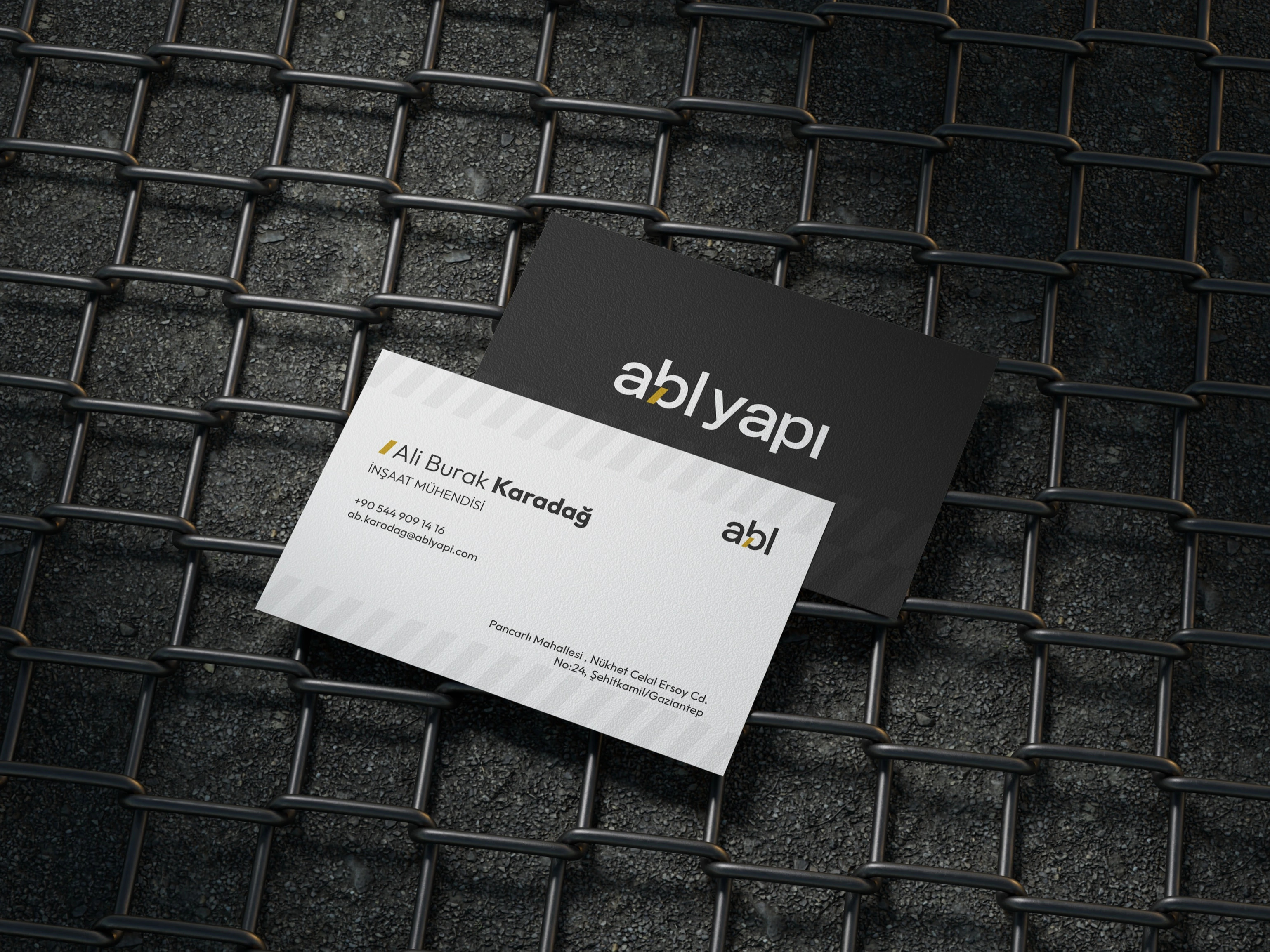 Black and white ABL Yapı business cards on a wire mesh; the white card carries a diagonal stripe pattern and the details of civil engineer Ali Burak Karadağ