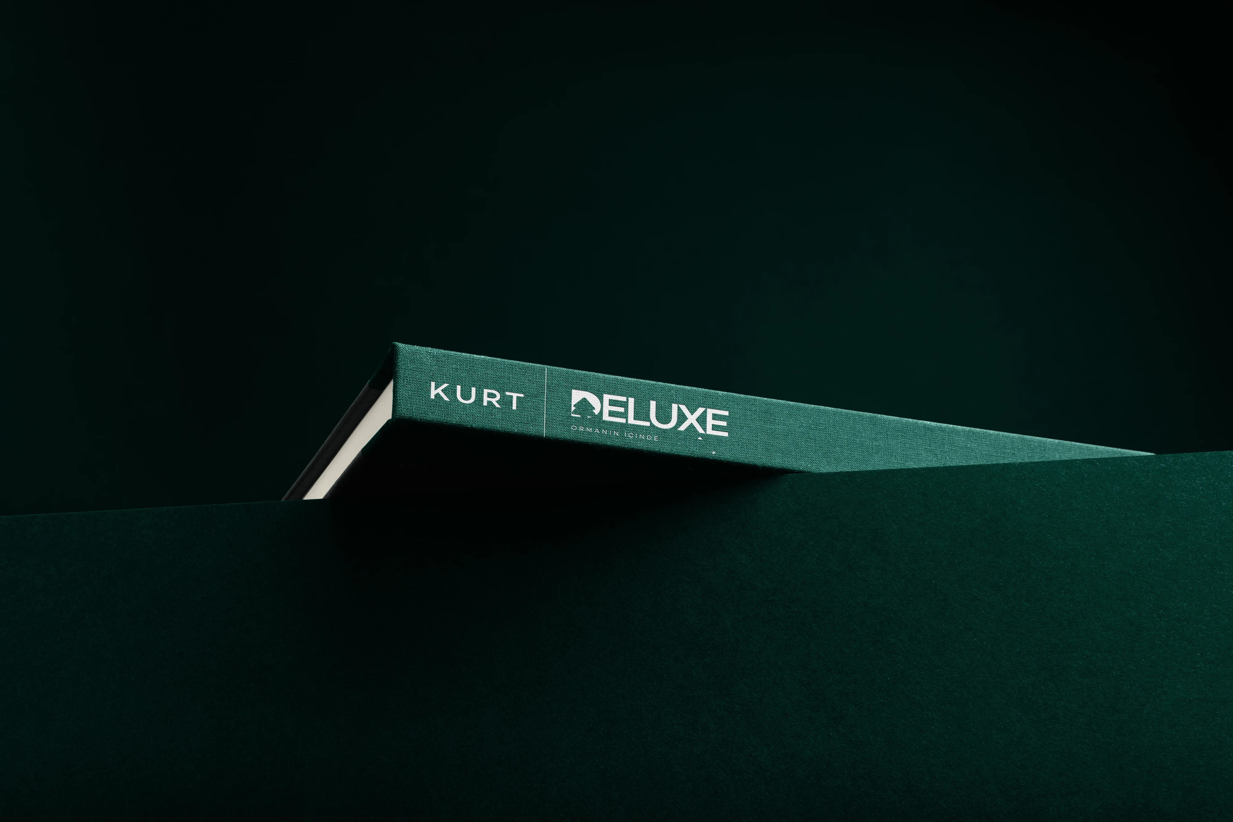 A green cloth-bound catalog carrying the Kurt Deluxe logo on its spine, against a deep green backdrop